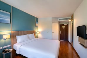A hotel room with a large bed, bedside lamps, a flat-screen TV, and a door leading to another room. - ibis Phuket Patong (Patong)