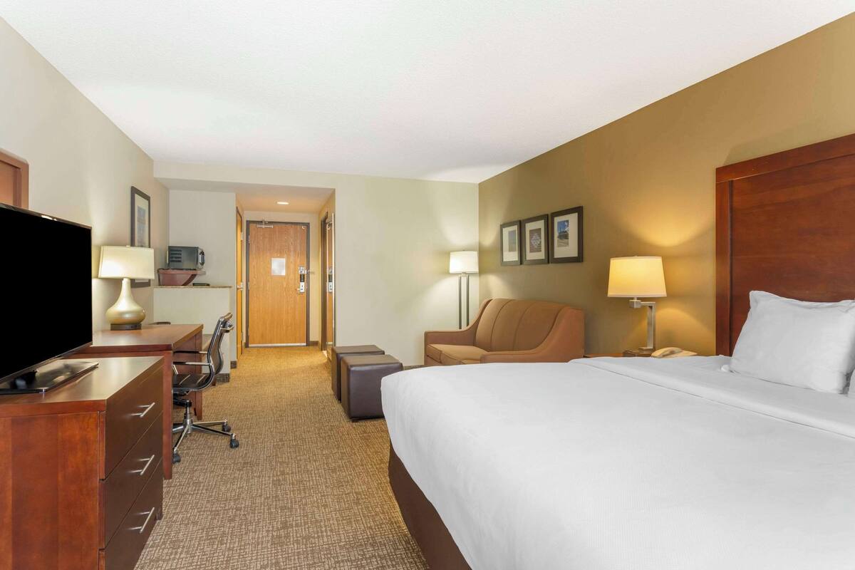 A hotel room with a bed, desk, chair, TV, and lamps.