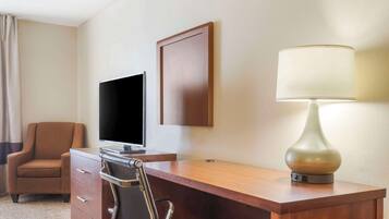 A hotel room with a wooden desk, a chair, a television, and a lamp.