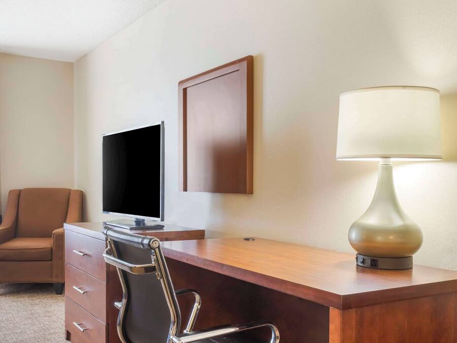 A hotel room with a wooden desk, a chair, a television, and a lamp.