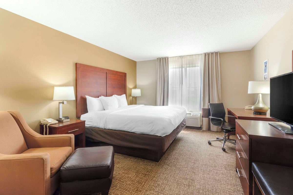 A hotel room with a large bed, a desk with a computer, a chair, a TV, and a telephone.