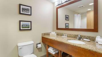A bathroom with a toilet, sink, and mirror. There are framed pictures on the wall.