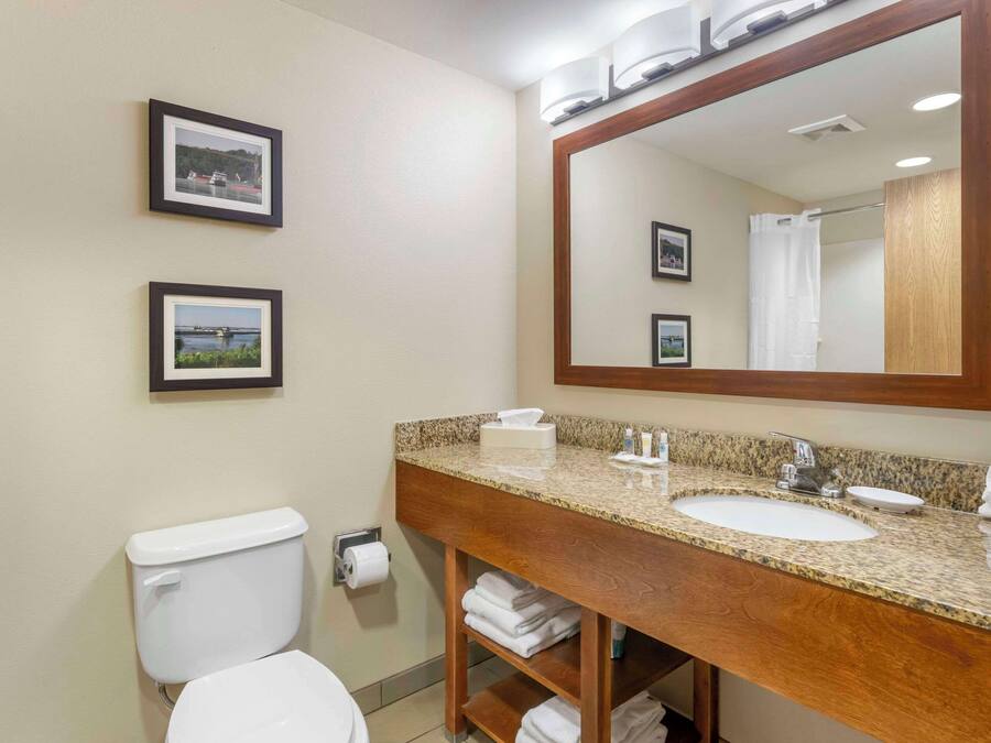 A bathroom with a toilet, sink, and mirror. There are framed pictures on the wall.