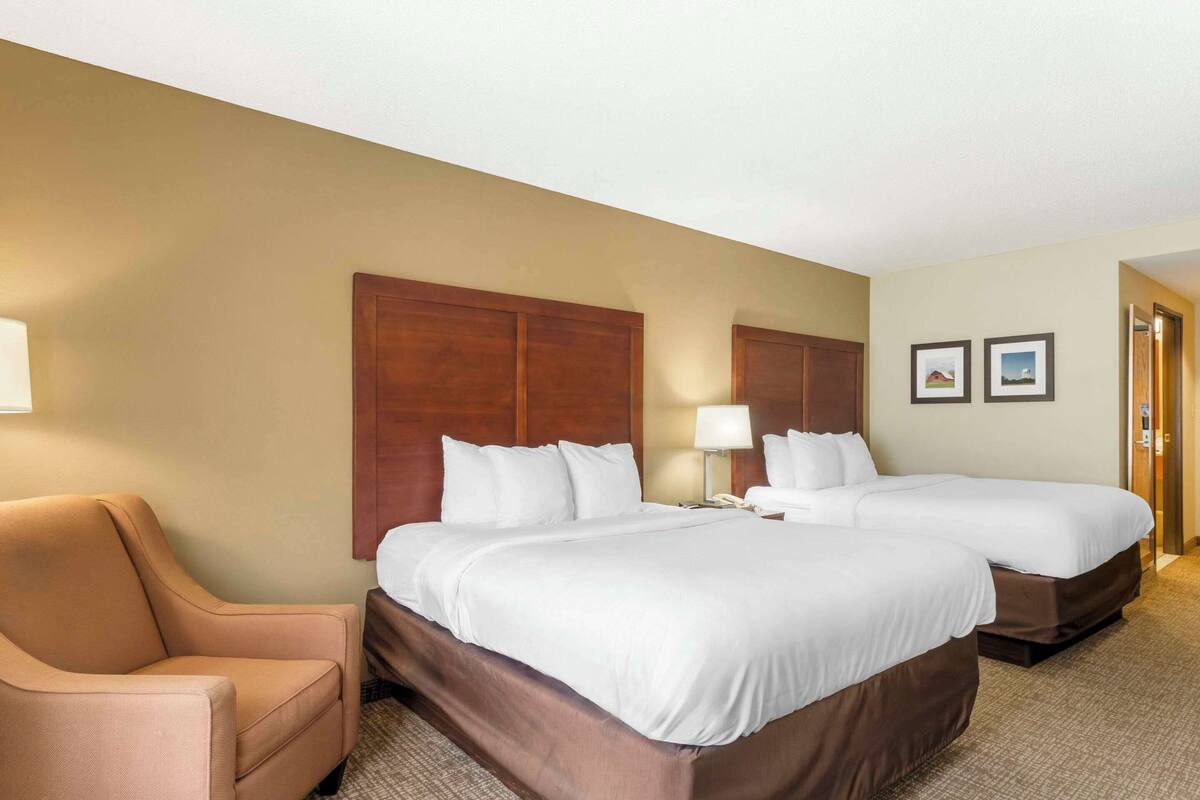 A hotel room with two beds, a chair, a desk, and a lamp.