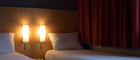 Habitación de hotel con dos camas, cada una con ropa de cama y almohadas blancas. Hay luces empotradas en la pared a ambos lados de las camas.