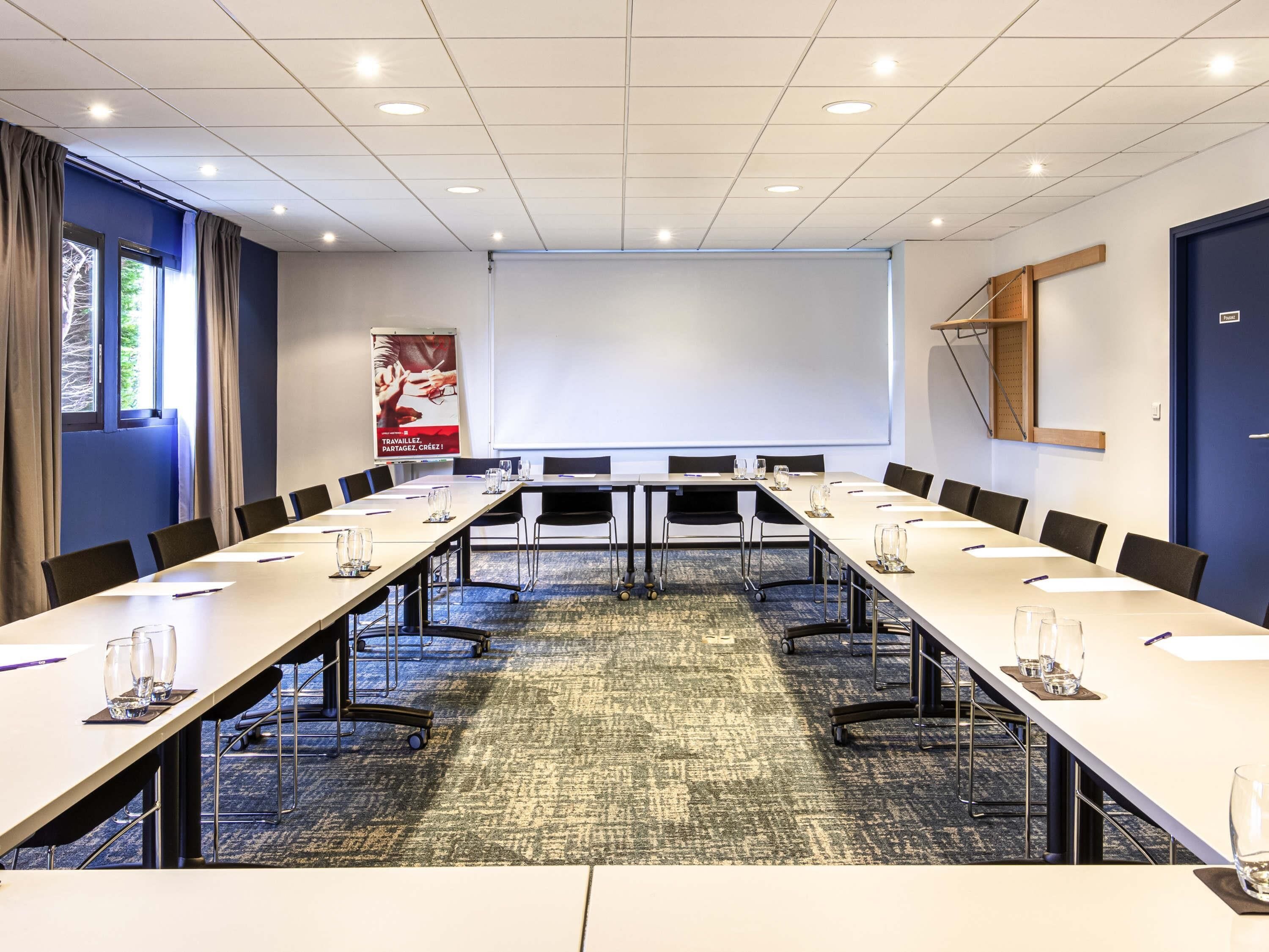 A conference room with a long table, chairs, a projector screen, and a carpeted floor.