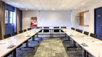 A conference room with a long table, chairs, a projector screen, and a carpeted floor.