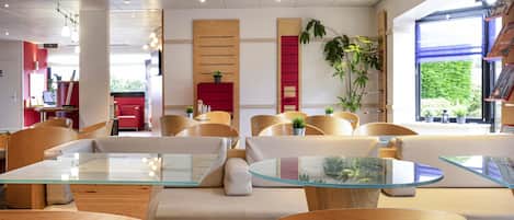 A modern hotel lobby with a seating area, wooden furniture, and a large window with a view of greenery.