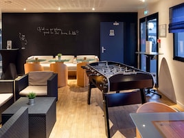 Un área de lounge moderna con mesa de fútbol, asientos cómodos y una pizarra con una pregunta en francés.