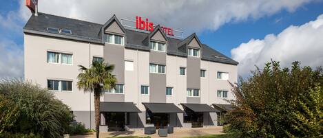 A modern hotel with a flat roof, multiple balconies, and a sign reading "ibis hotel".