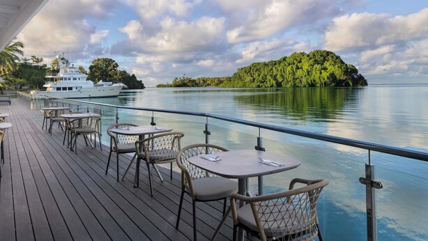 A deck with tables and chairs, overlooking a calm body of water and a forested island. - Novotel Suva Lami Bay (Suva)