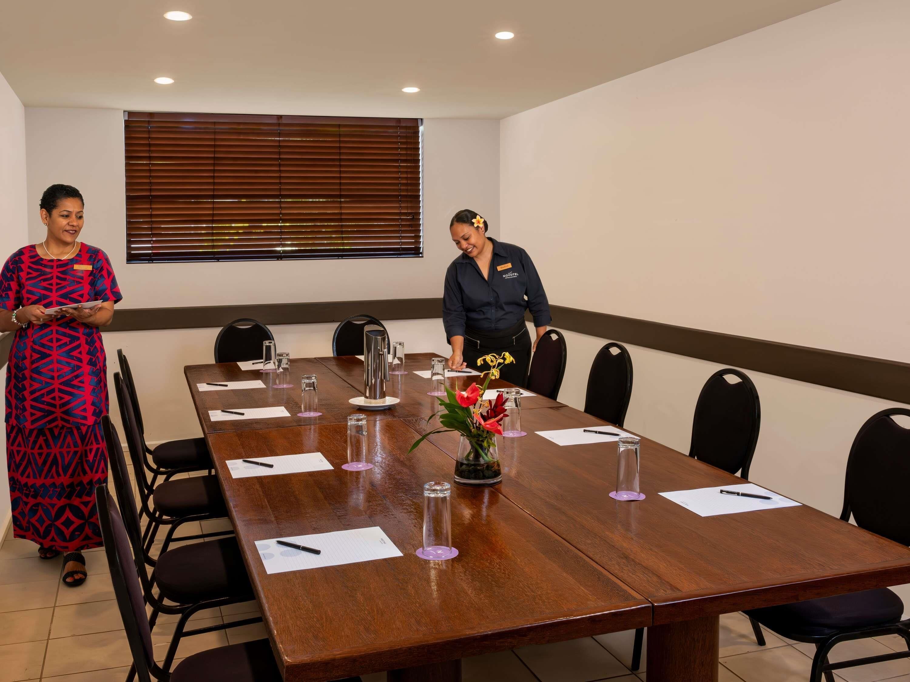 A conference room with a long table, chairs, name tags, and a window with blinds.
