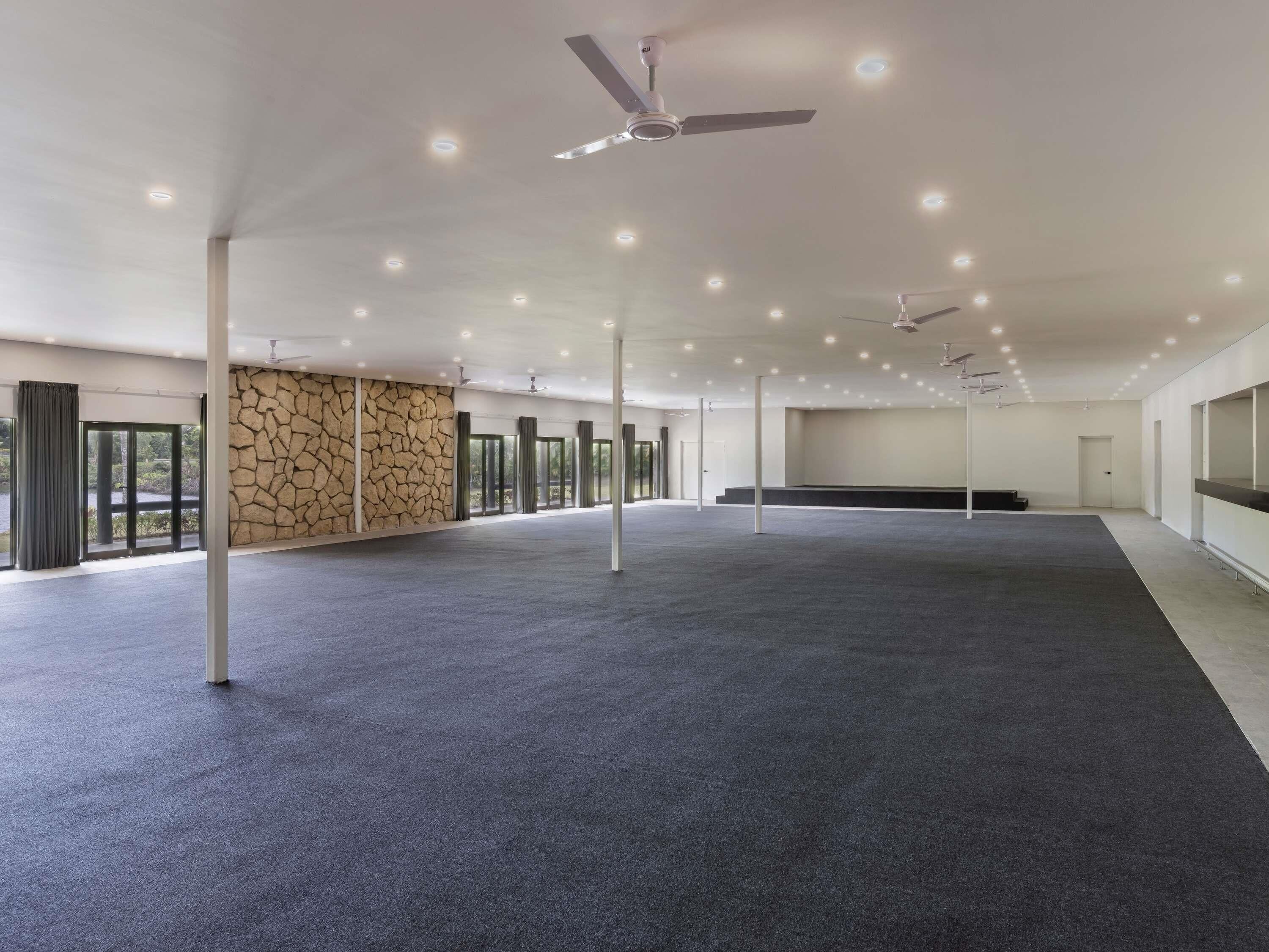 A spacious indoor area with a stone wall, large windows, and ceiling fans.