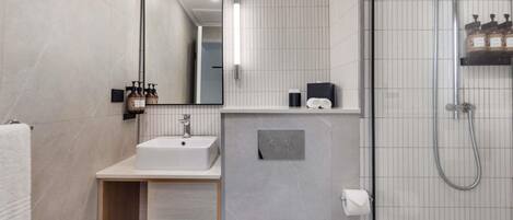 A modern bathroom with a white sink, mirror, and shower. There are towels and toiletries on the counter.