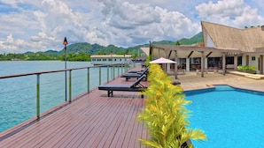A wooden deck with lounge chairs, a pool, and a building with a sloped roof. - Novotel Suva Lami Bay (Suva)