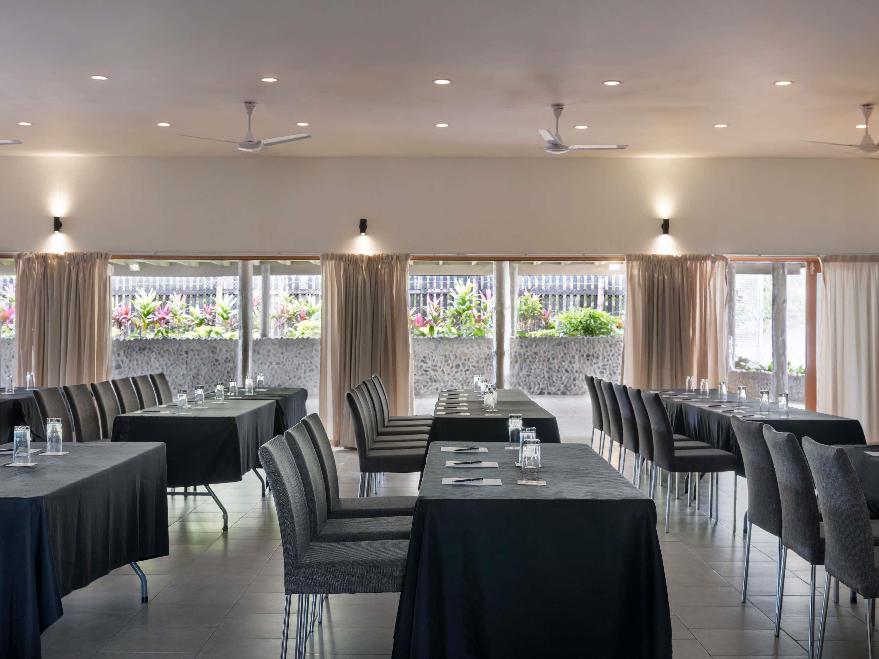 A restaurant with multiple tables and chairs, ceiling fans, and large windows with curtains.