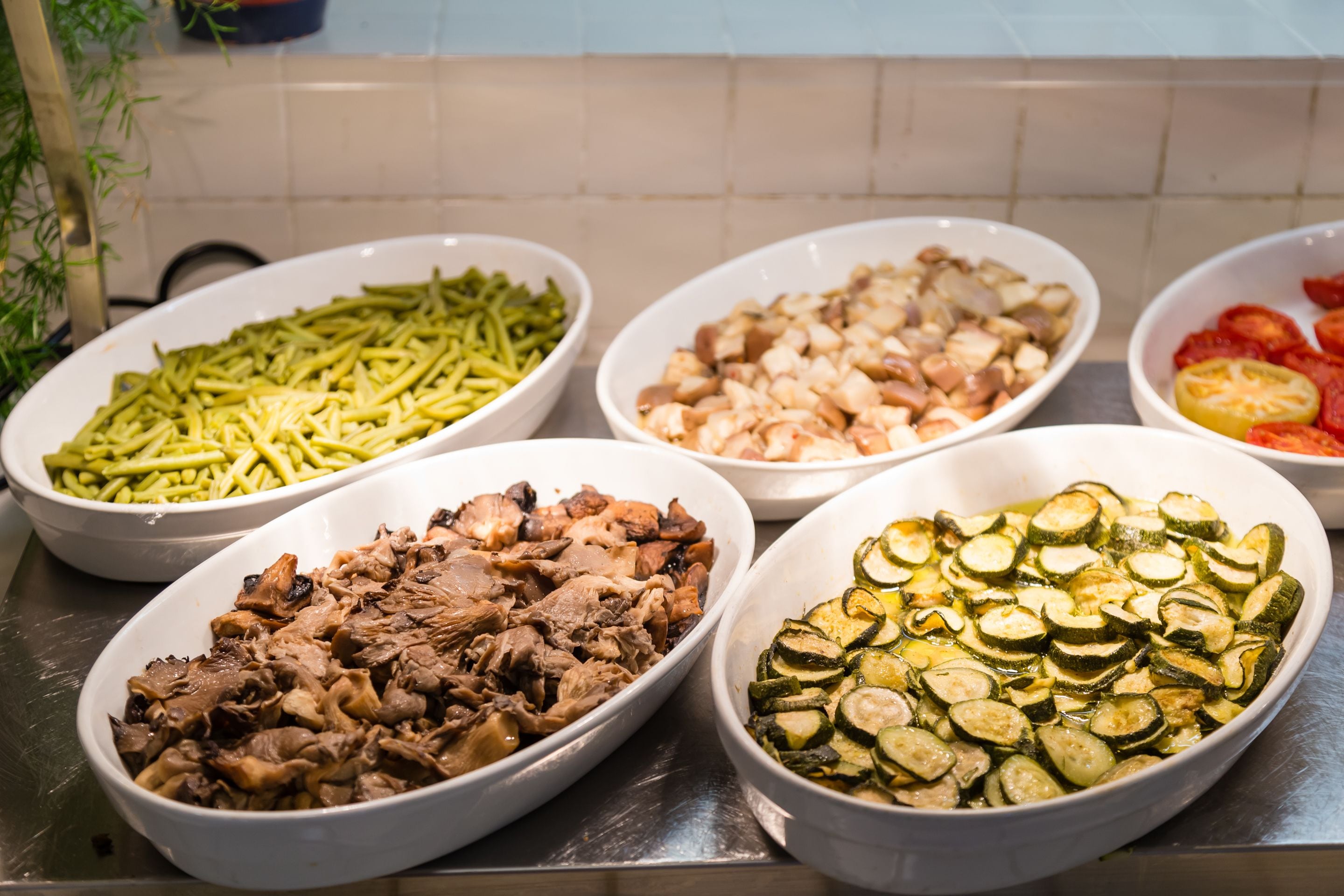 A buffet with various dishes including green beans, chicken, and sliced zucchini.