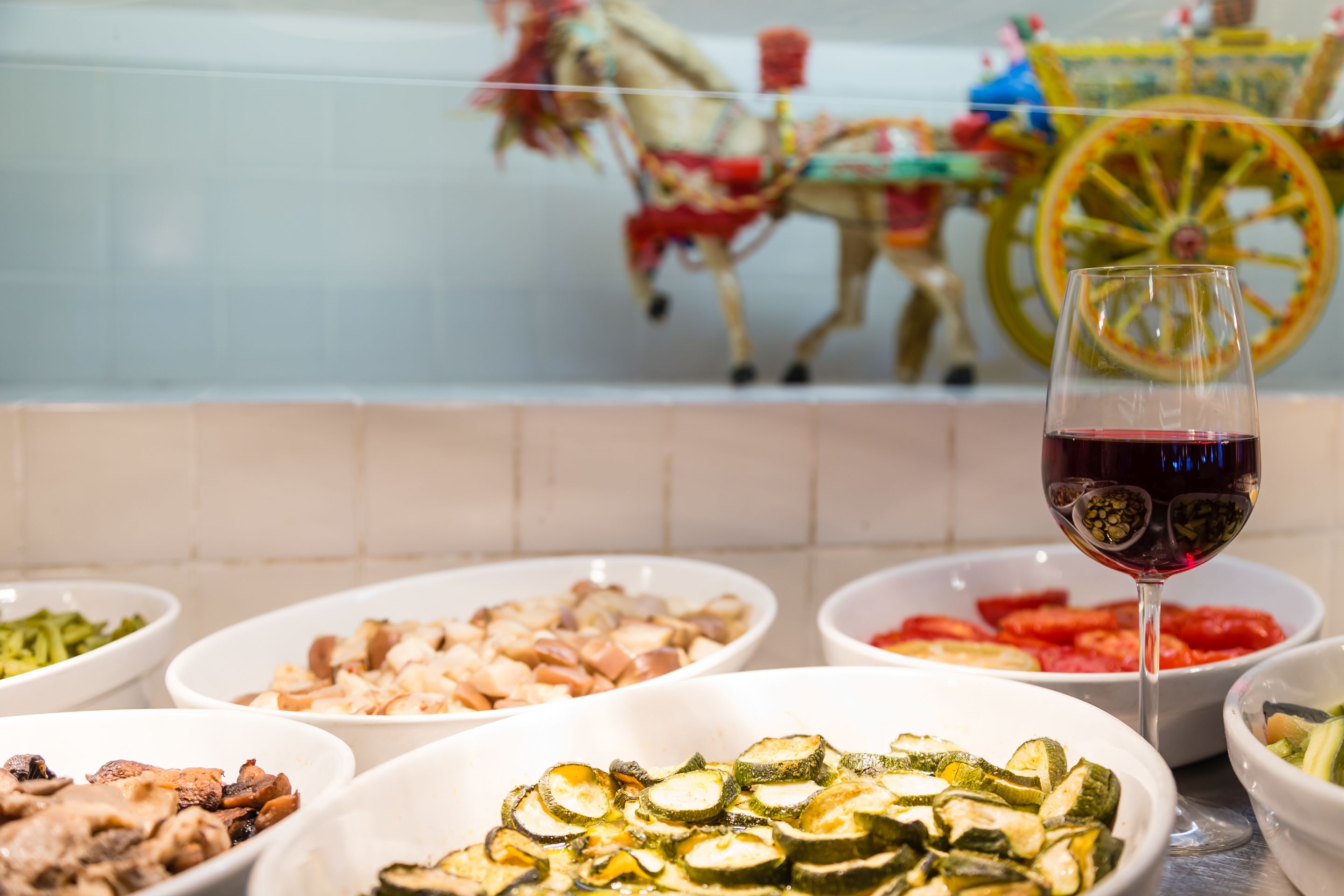 Una mesa con varios platos y una copa de vino tinto.