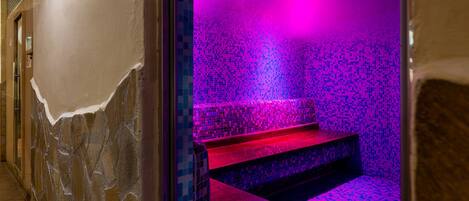 Une salle de bain aux murs en pierre, dotée d’un sol carrelé et d’un banc.