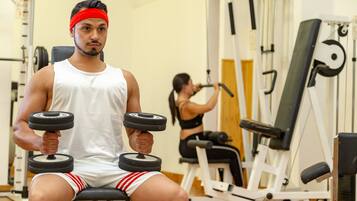 Ein Fitnessstudio mit Trainingsgeräten, darunter eine Hantelbank und ein Kabelzuggerät.