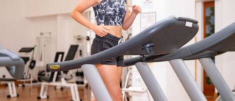A woman running on a treadmill in a gym with exercise equipment and clocks on the wall.