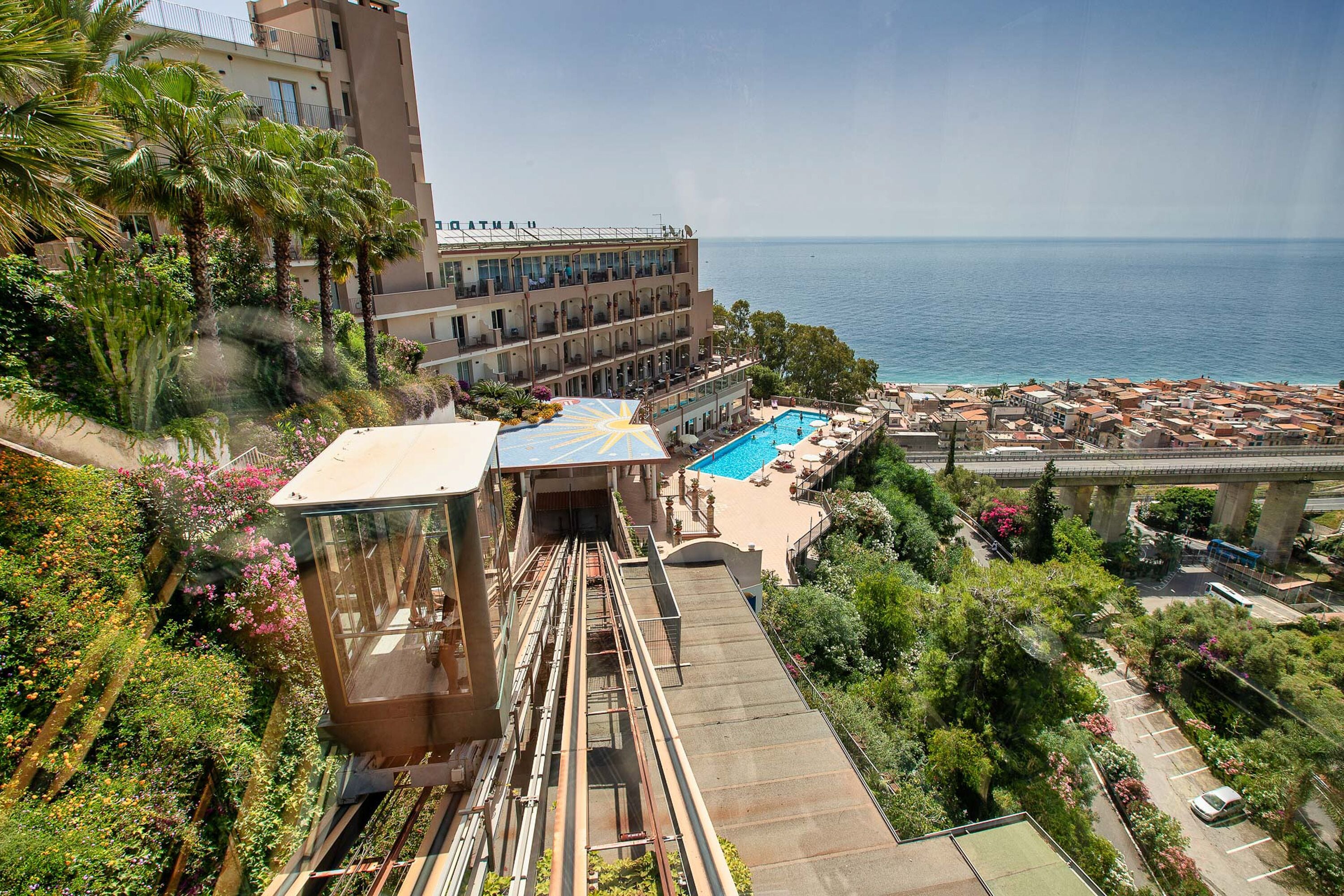 A hotel with a pool, a view of the sea, and a cable car system.