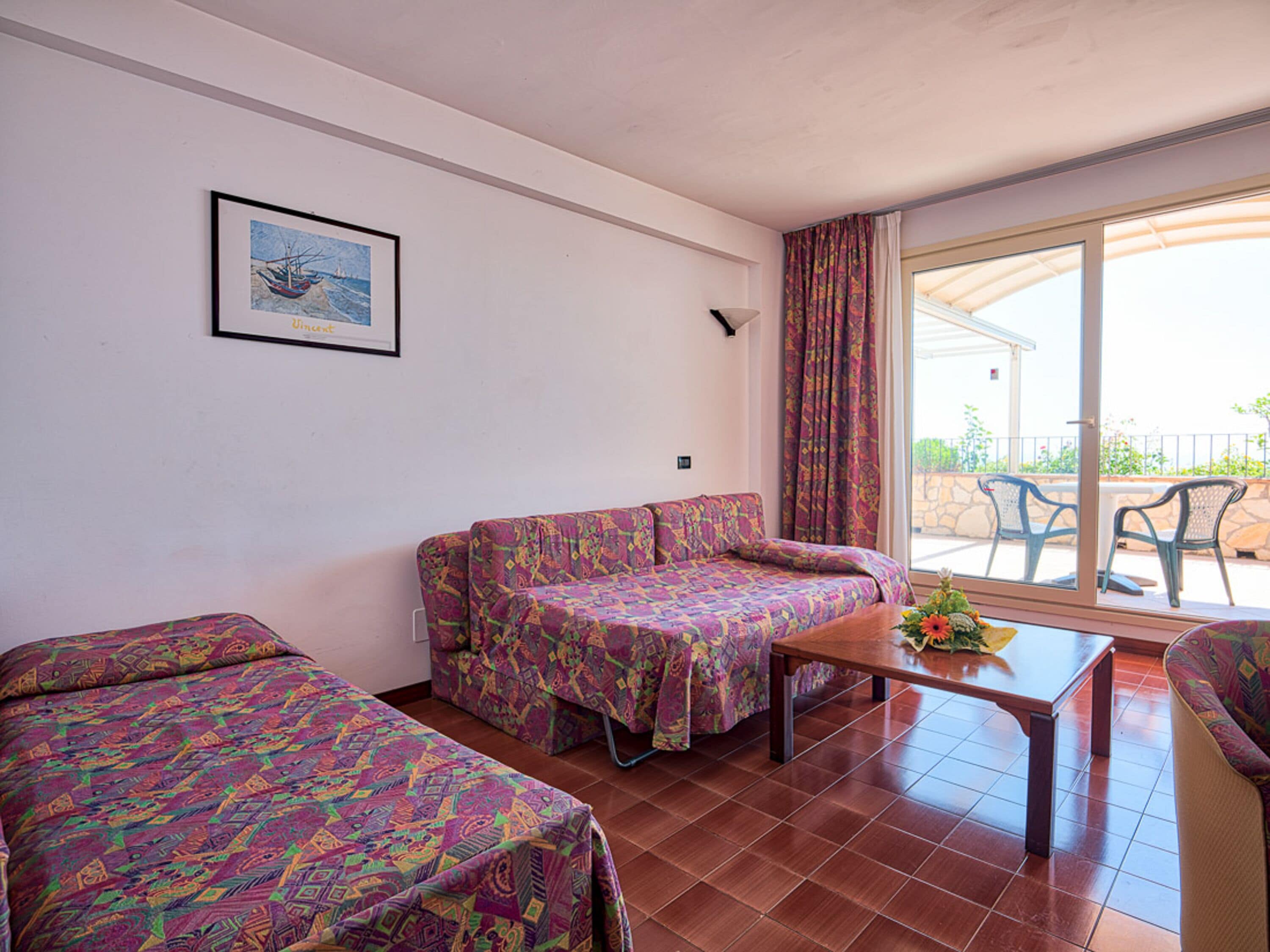A room with a sofa, a small table, and a chair. There is a window with curtains and a view of the outside.