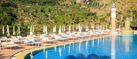 Zona de piscina con sillas de descanso y sombrillas, rodeada de un paisaje montañoso.