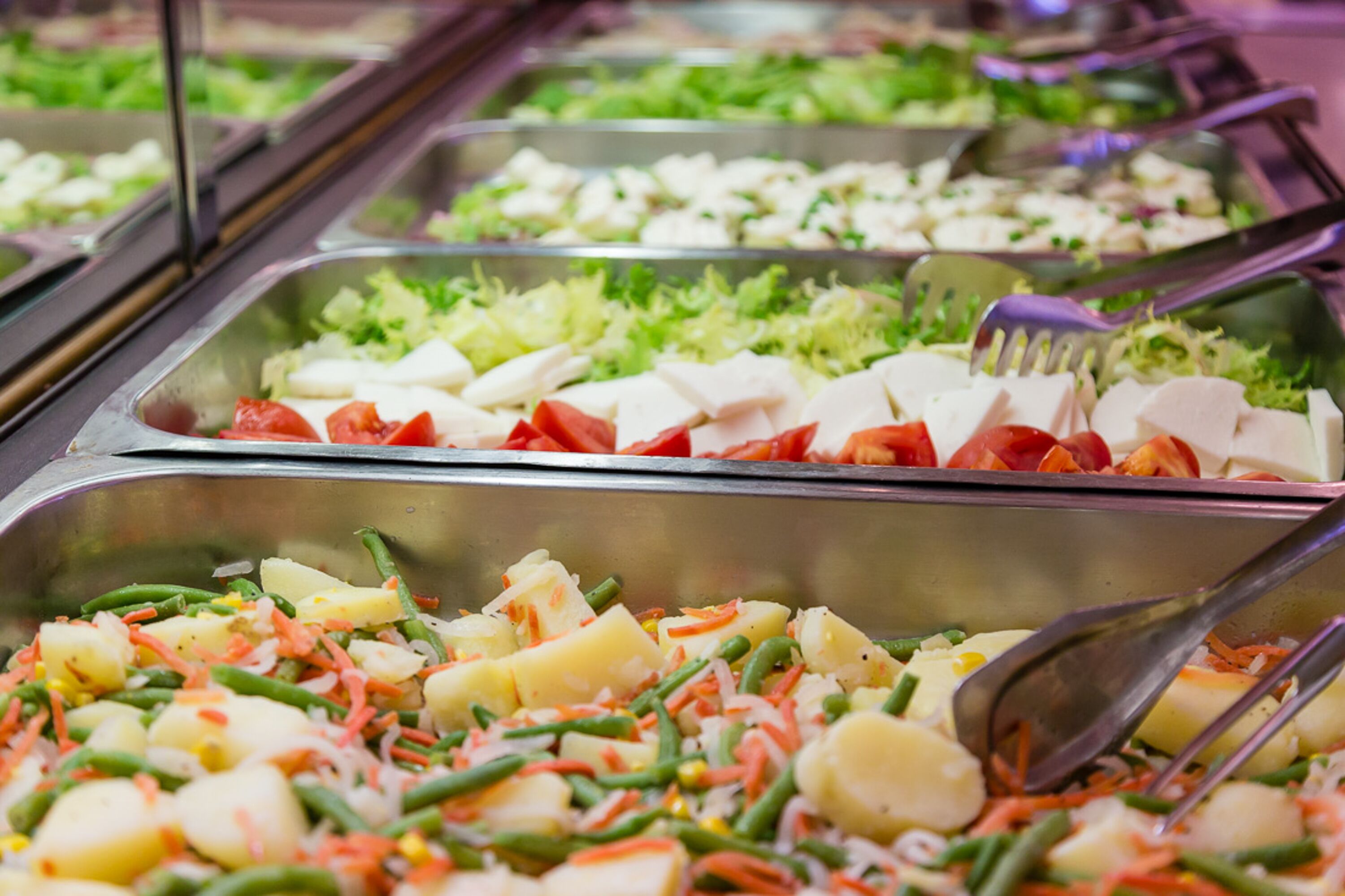 Un bufé con diversas opciones de comida, como ensaladas, verduras y queso.