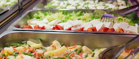 Un bufé con diversas opciones de comida, como ensaladas, verduras y queso.