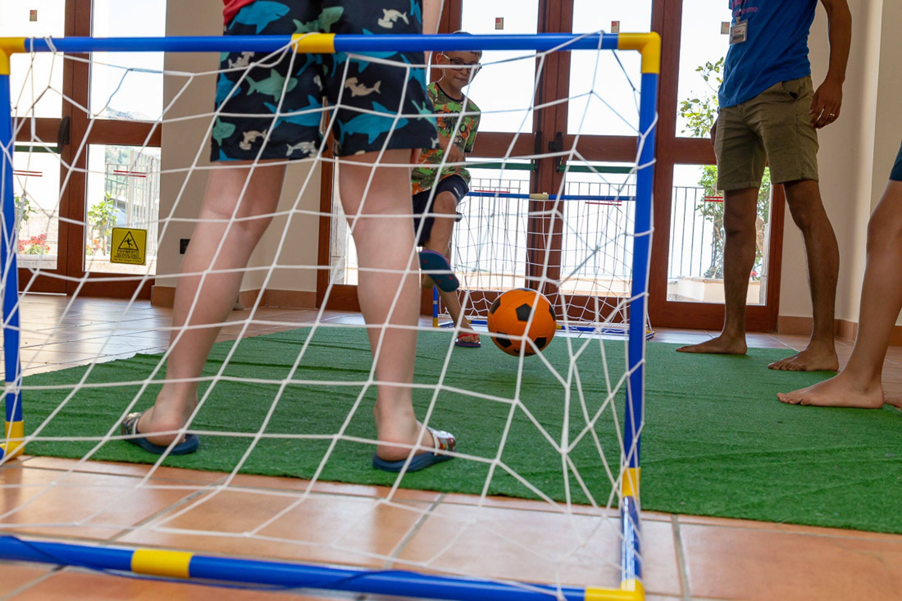 A soccer goal with a net, a green artificial turf, and a yellow caution sign.