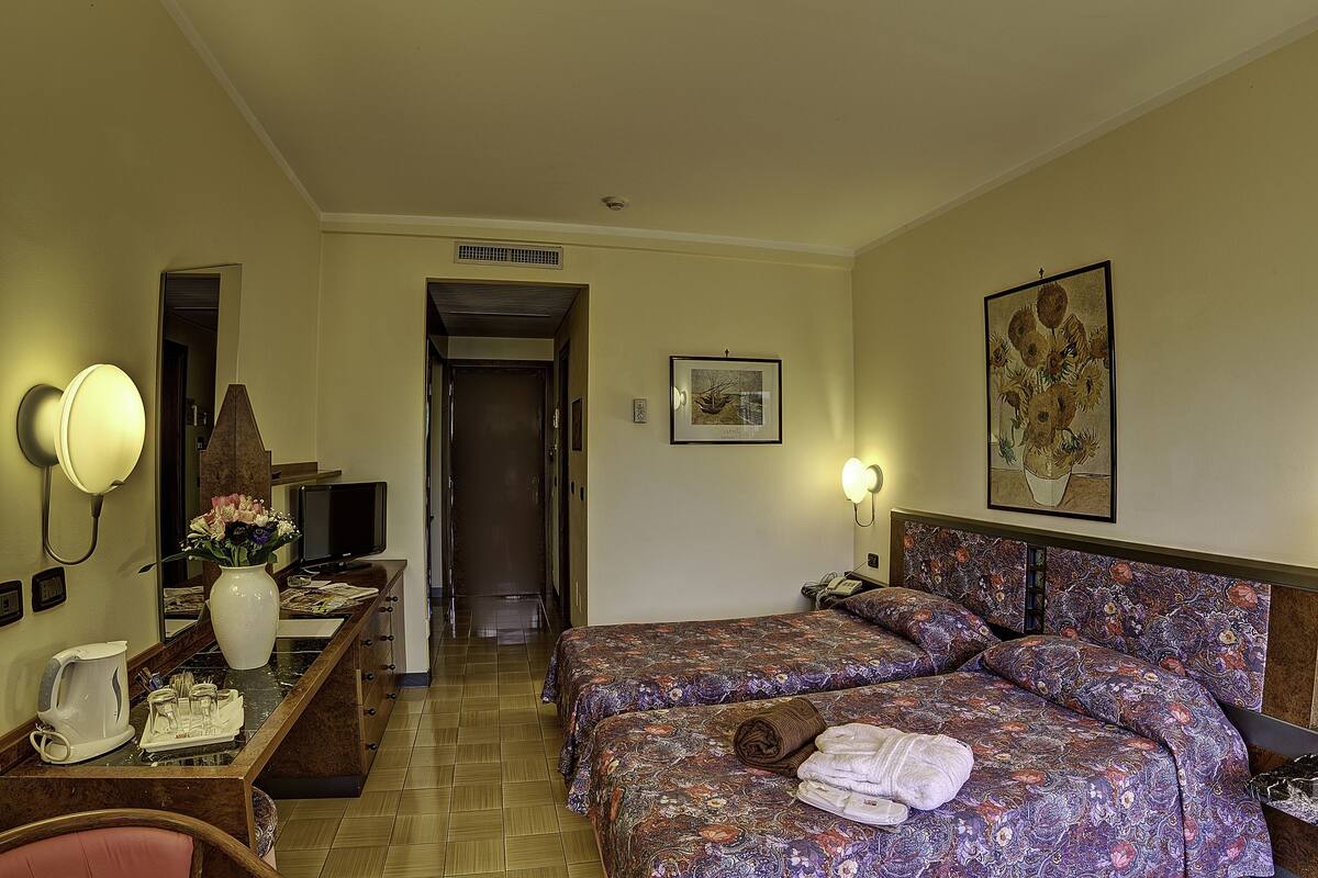 Une chambre d’hôtel avec un lit, un bureau doté d’une lampe, une chaise, un téléviseur et un tableau au mur.