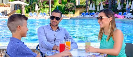 Un área de comedor junto a la piscina con mesa y sillas, una piscina y sillones de descanso al fondo.