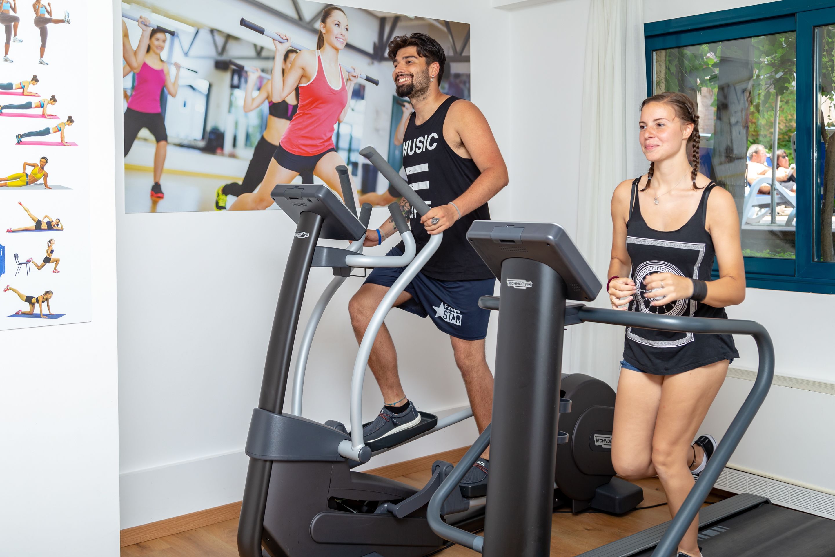 A gym with treadmills, a wall with fitness images, and a window with a view of people outside.