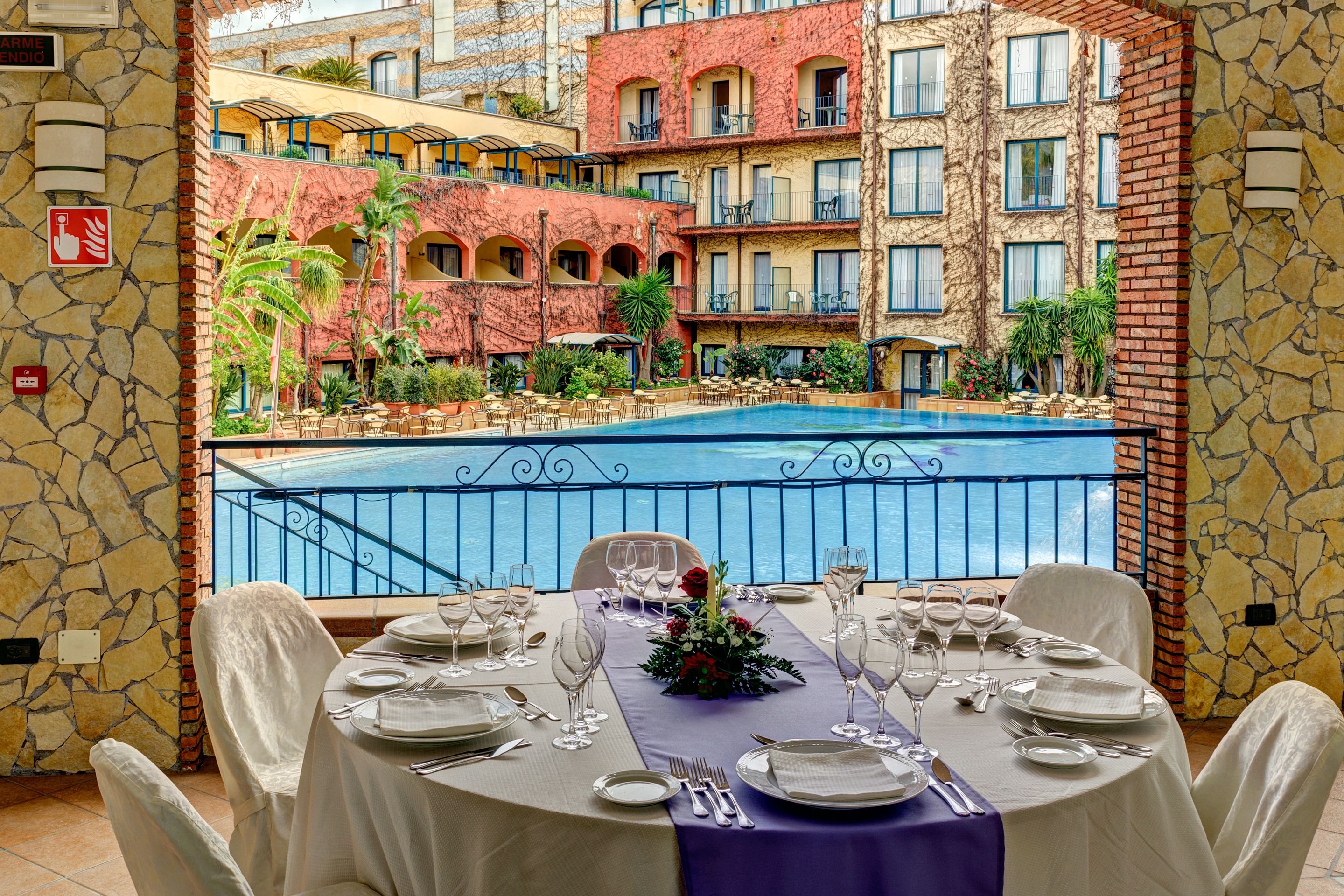 A dining area with a table set for a meal, overlooking a pool and a building with multiple balconies.