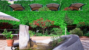 Un patio con fuente, plantas en macetas y pared cubierta de vegetación.