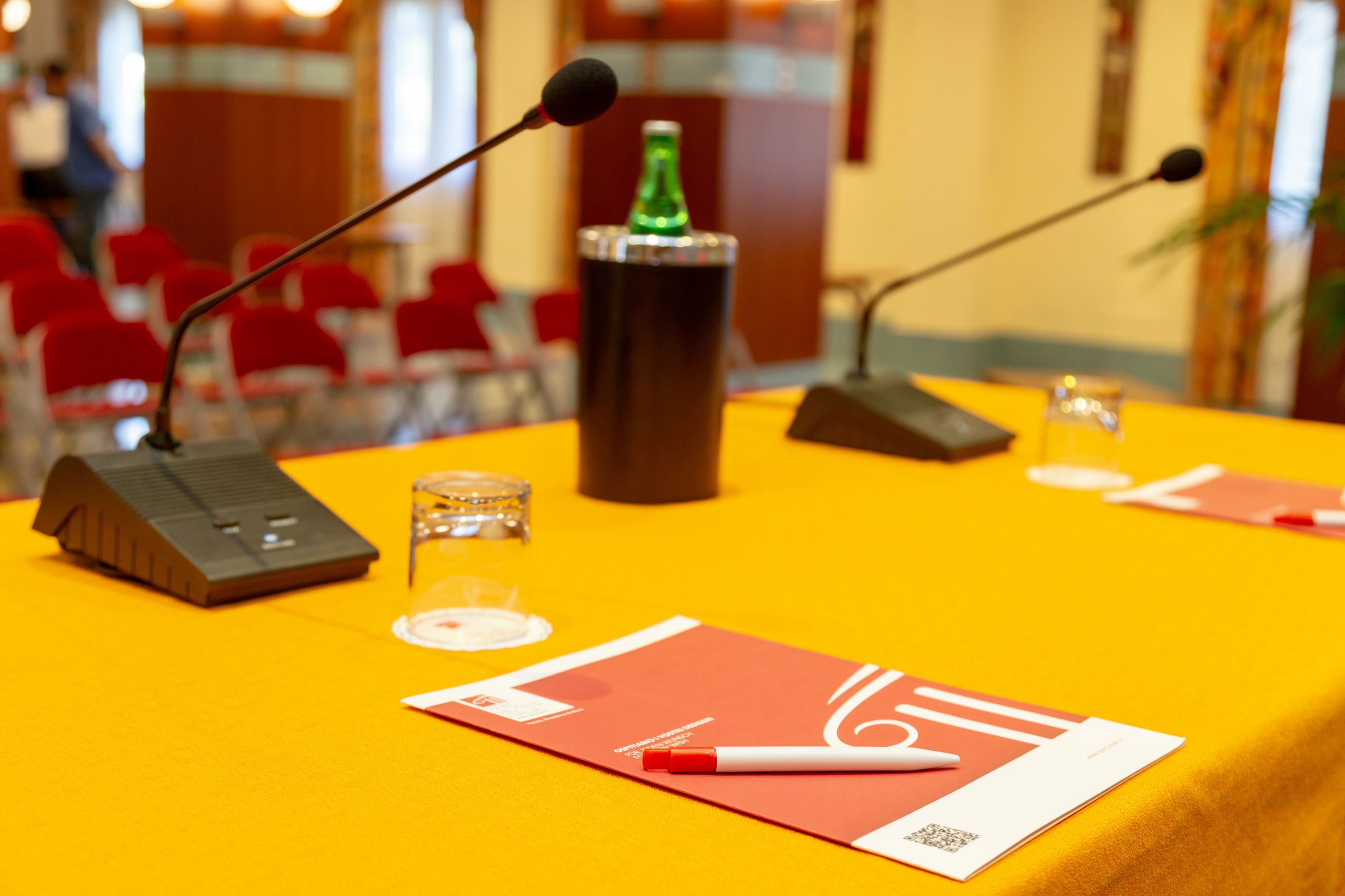 Une table de conférence avec des microphones, une bouteille et des documents.