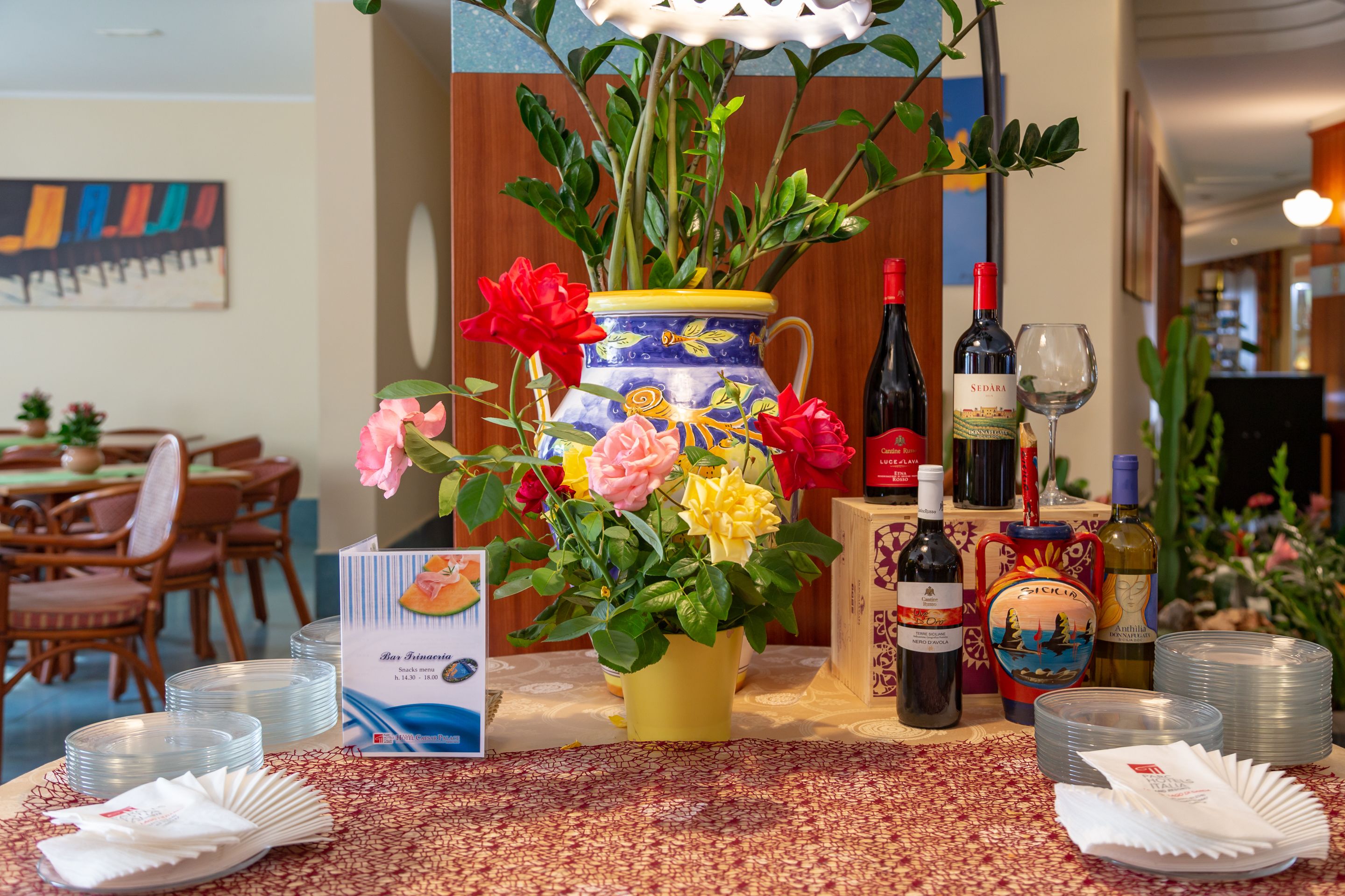 A dining area with a table set for a meal, a vase with flowers, and wine bottles.