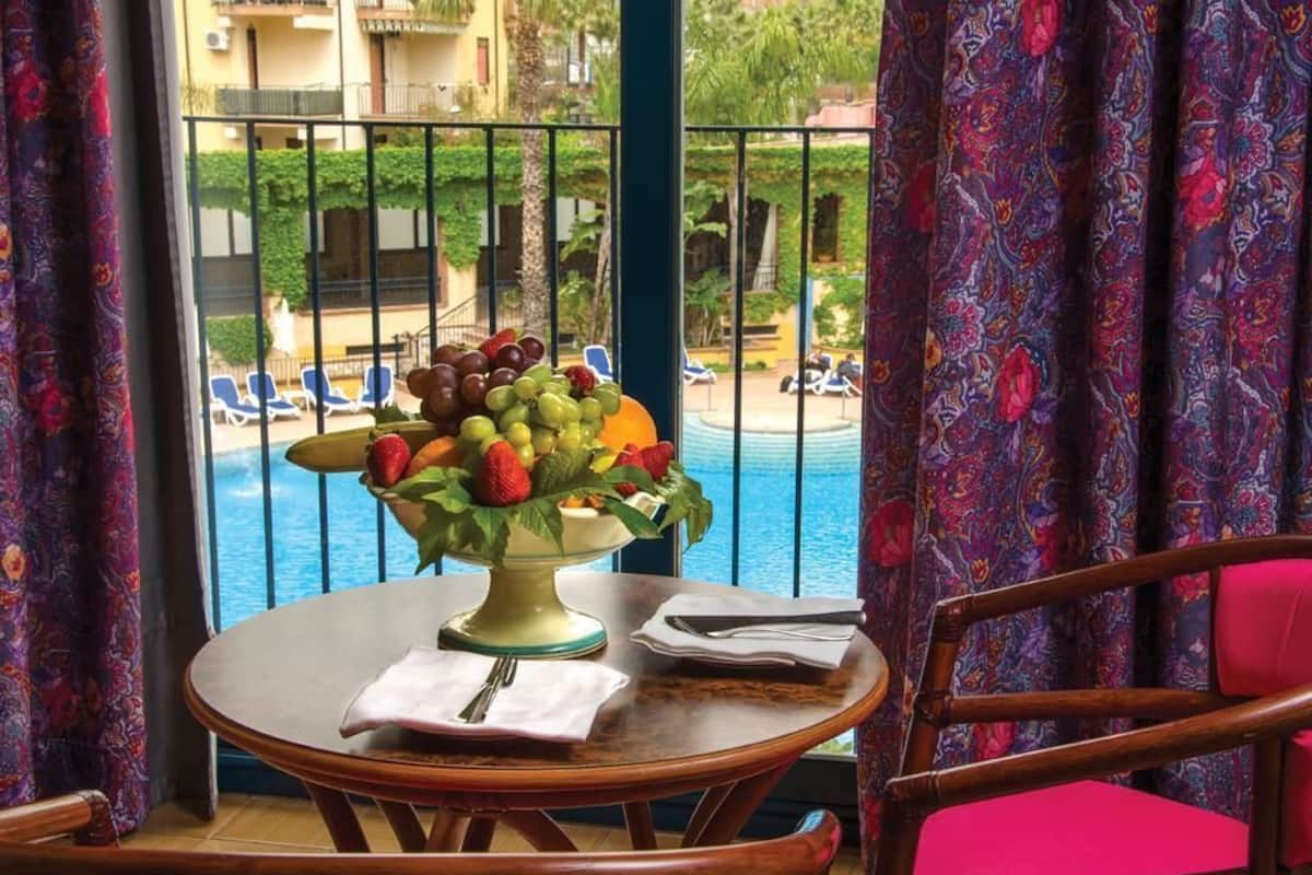 Une table à manger agrémentée d’un centre de table composé de fruits, une chaise, et une vue sur une piscine et des bâtiments.