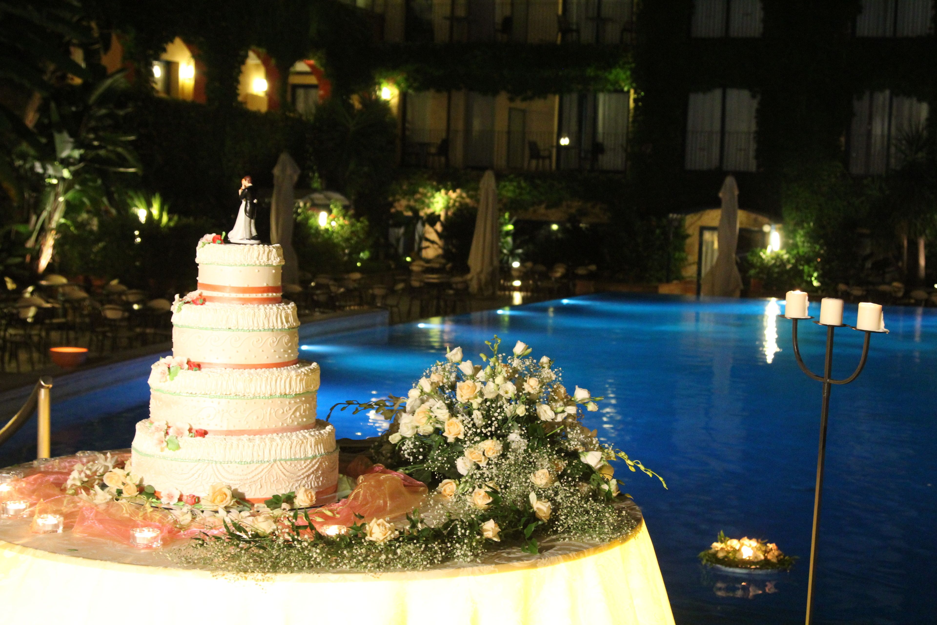 Un pastel de bodas de varios niveles con adornos florales sobre una mesa junto a una piscina.