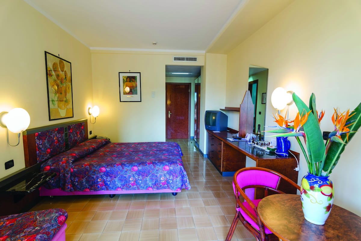 Une chambre d’hôtel avec un lit, un bureau, une chaise, un vase de fleurs et des lampes fixées au mur.