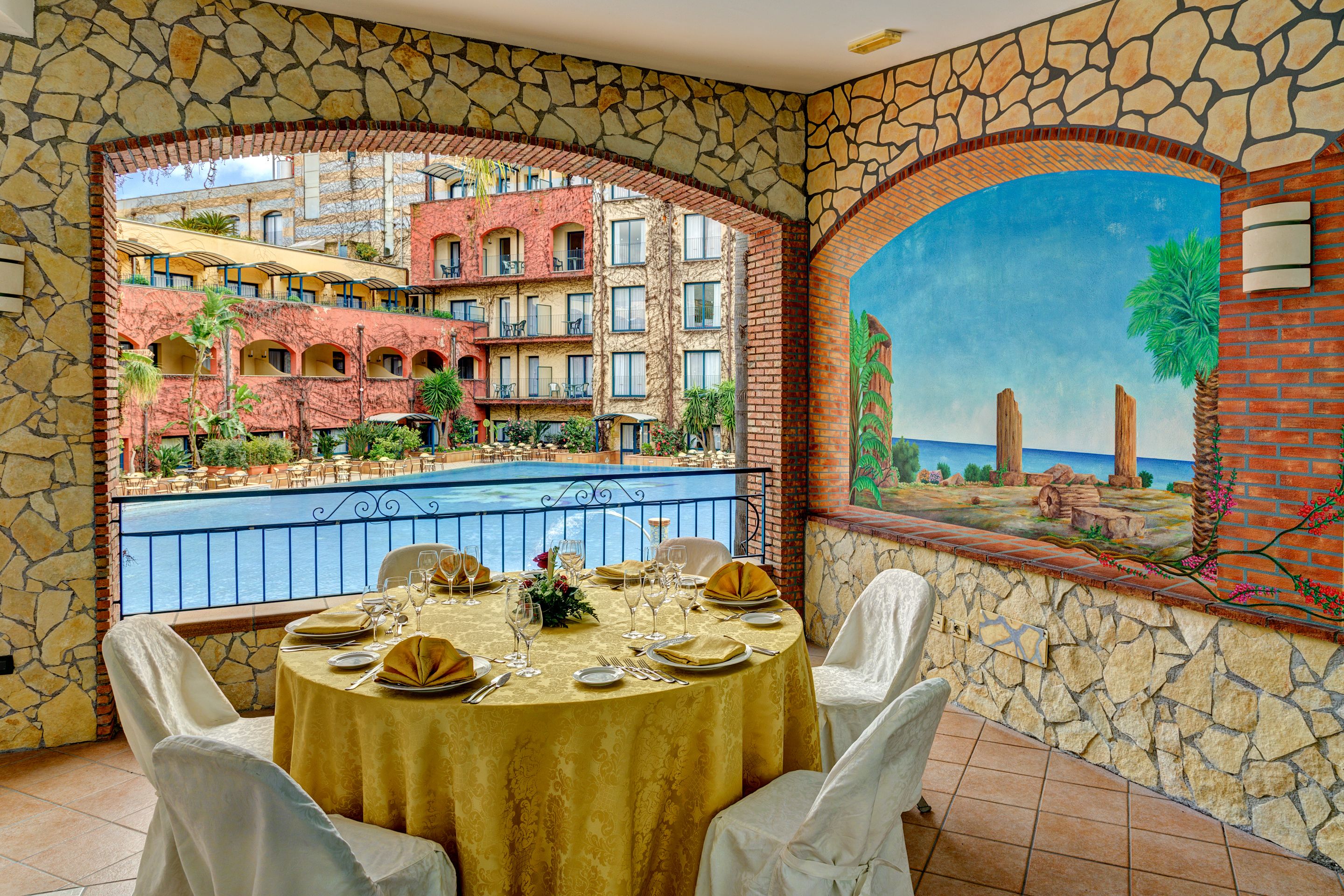 A dining area with a table set for four, overlooking a pool and a building with balconies.