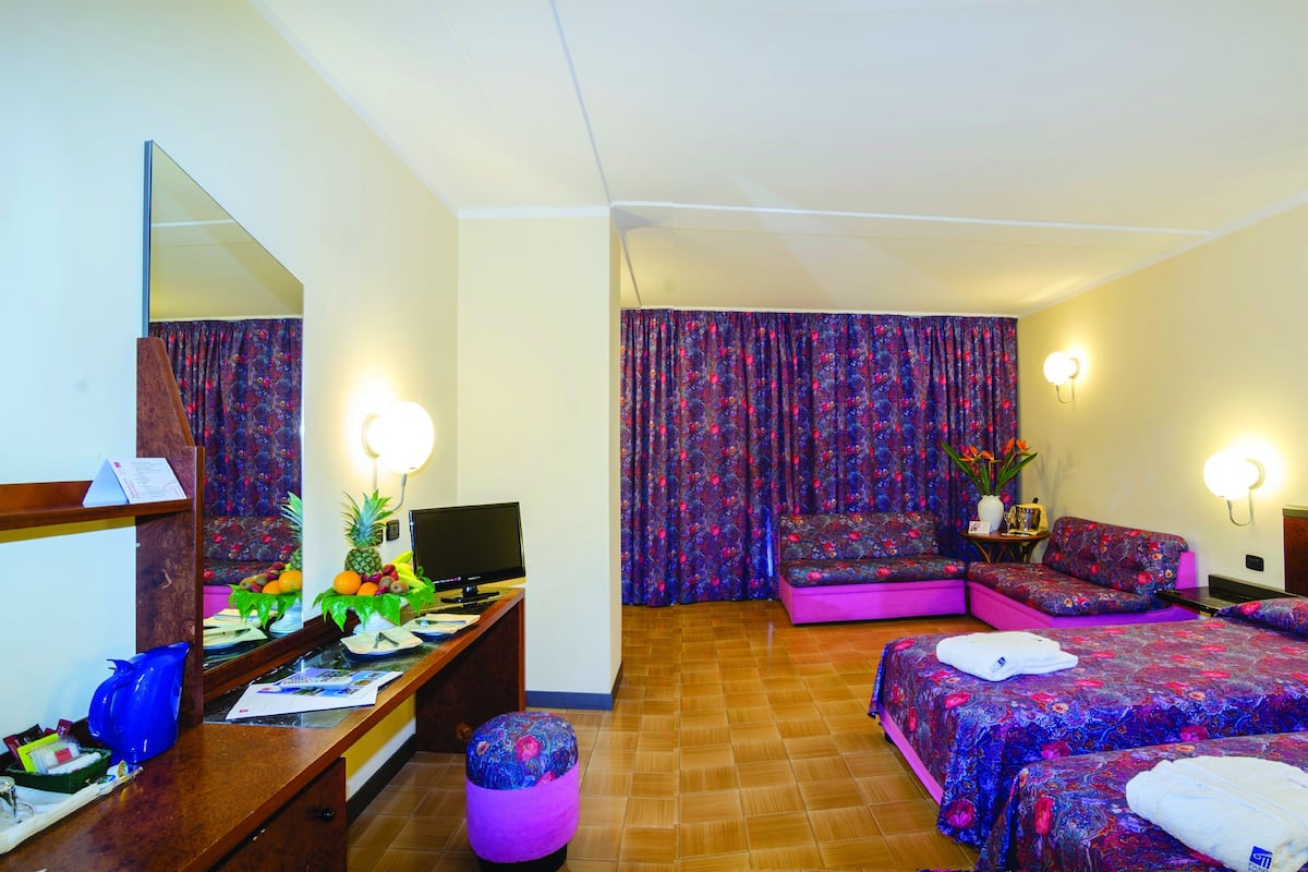 Une chambre d’hôtel avec deux lits, un bureau avec un ordinateur, un miroir et une fenêtre avec des rideaux.