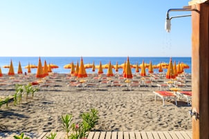A beach with rows of orange and yellow umbrellas and white lounge chairs.