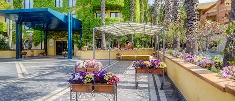 Un patio con una zona de estar cubierta, macetas de flores y un edificio cubierto de hiedra verde.