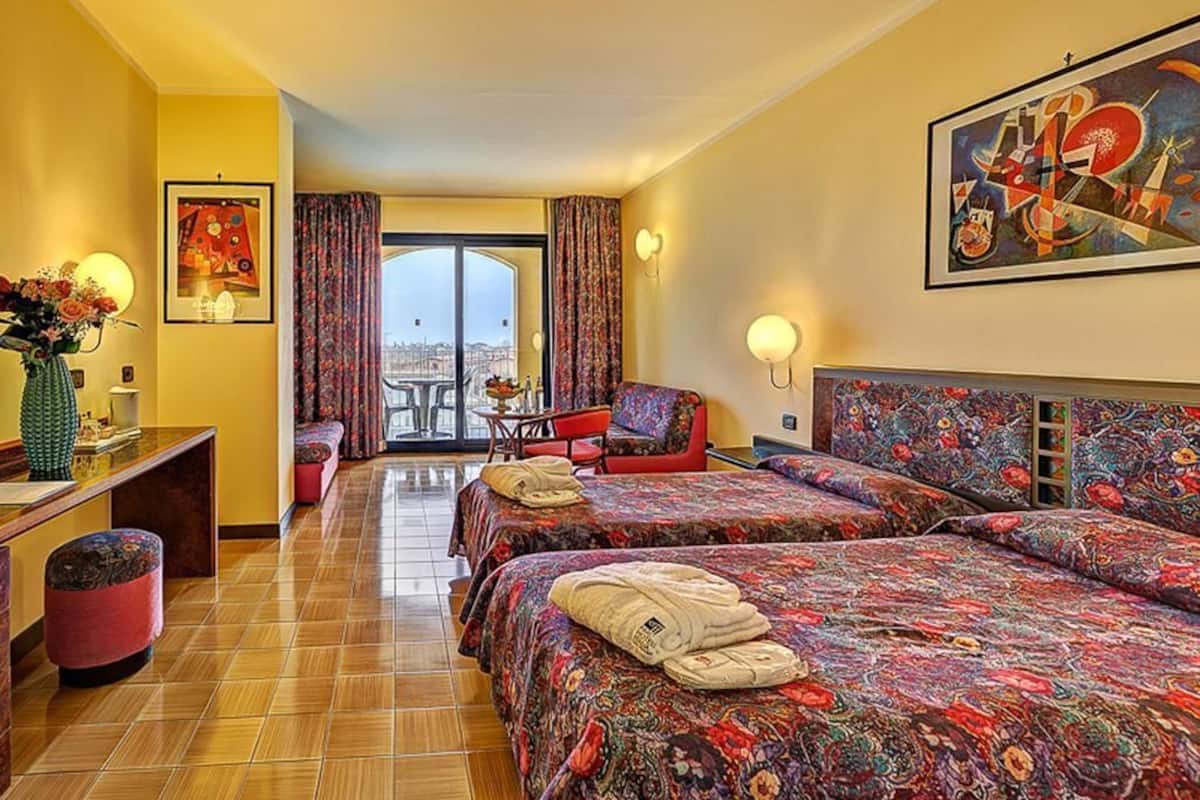 Une chambre d’hôtel avec deux lits, un bureau, une chaise, une petite table et une vue sur la ville.