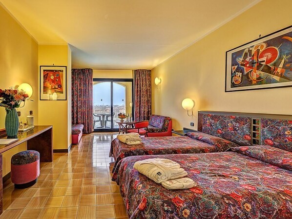 A hotel room with two beds, a desk, a chair, a small table, and a view of the city. - Hotel Caesar Palace (Giardini Naxos)