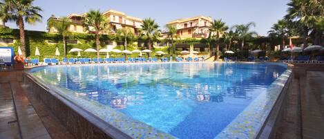 A swimming pool with blue tiles, surrounded by palm trees and blue lounge chairs.