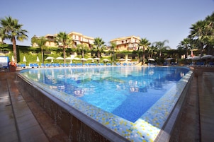 Una piscina con baldosas azules, rodeada de palmeras y sillas reclinables azules.