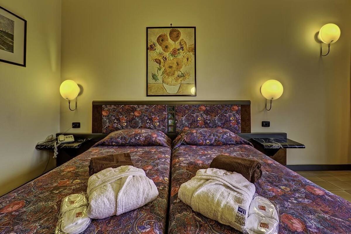 Un lit double avec une literie à motifs floraux, deux tables de chevet avec des lampes et une œuvre d’art encadrée au-dessus du lit.